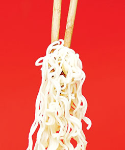 photo of chopsticks holding noodles against a red background