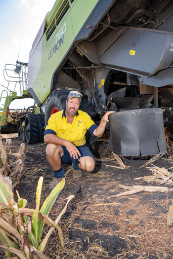 Peter Bach kneeling next to a chaff deck on a header in a paddock. He is smiling at the camera.