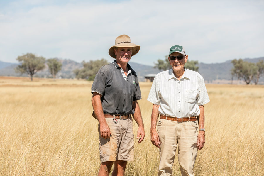 A photo of Gavin and Jim standing in a dry grassy paddock next to each other smiling at the camera.