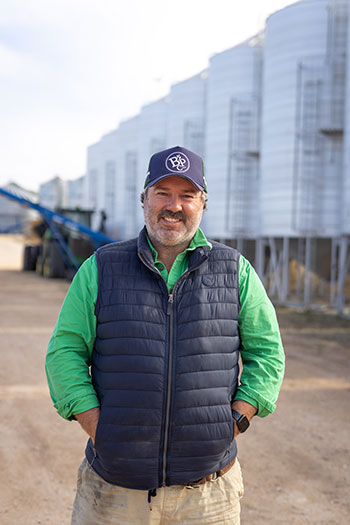 Man with hands in pockets standing in front of silos