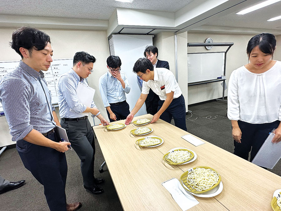 People standing around a table that has plates of noodles on it.